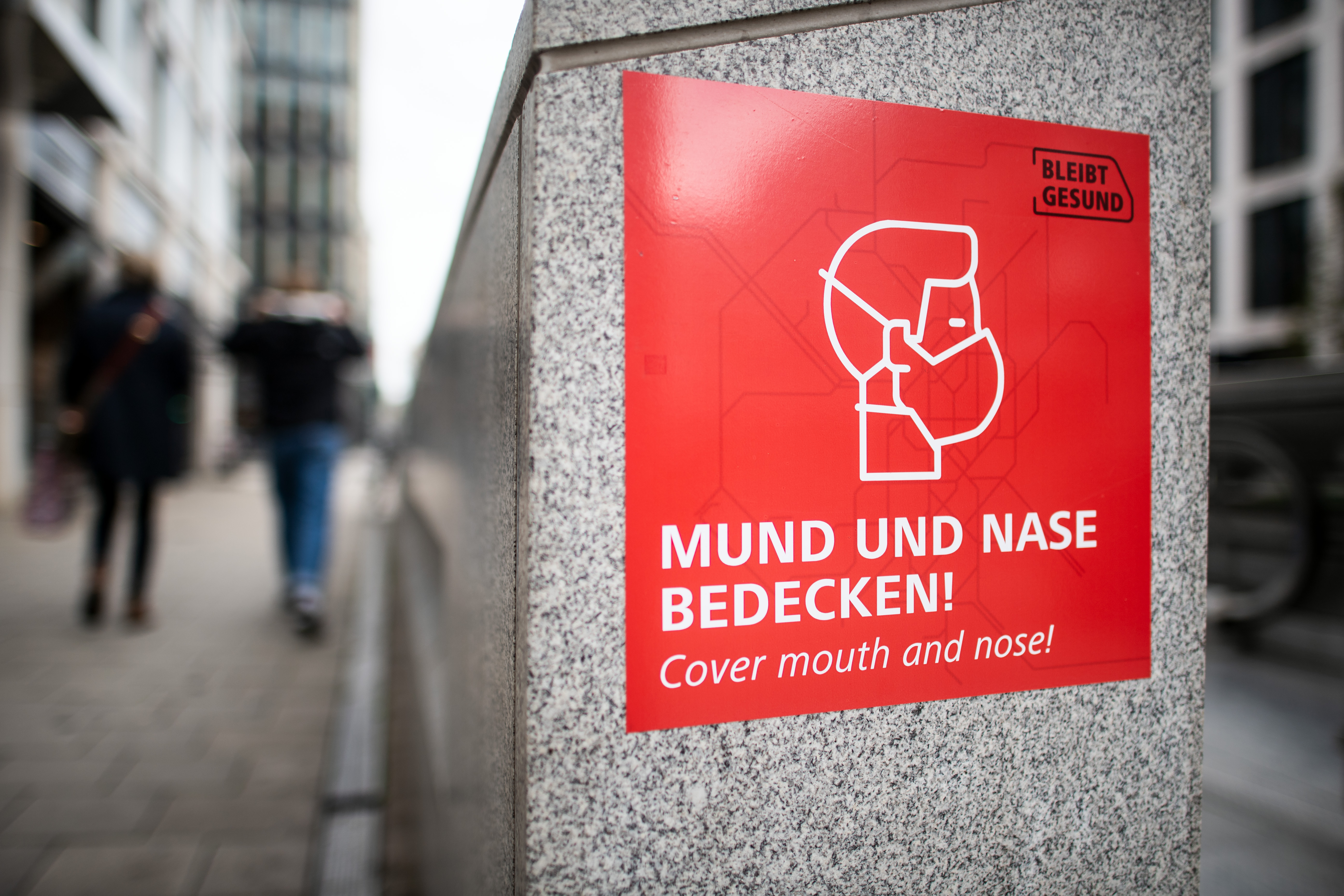 Ein Schild mit einem Piktogramm und dem Aufdruck "Mund und Nase bedecken" weist auf das Tragen von Schutzmasken hin. 