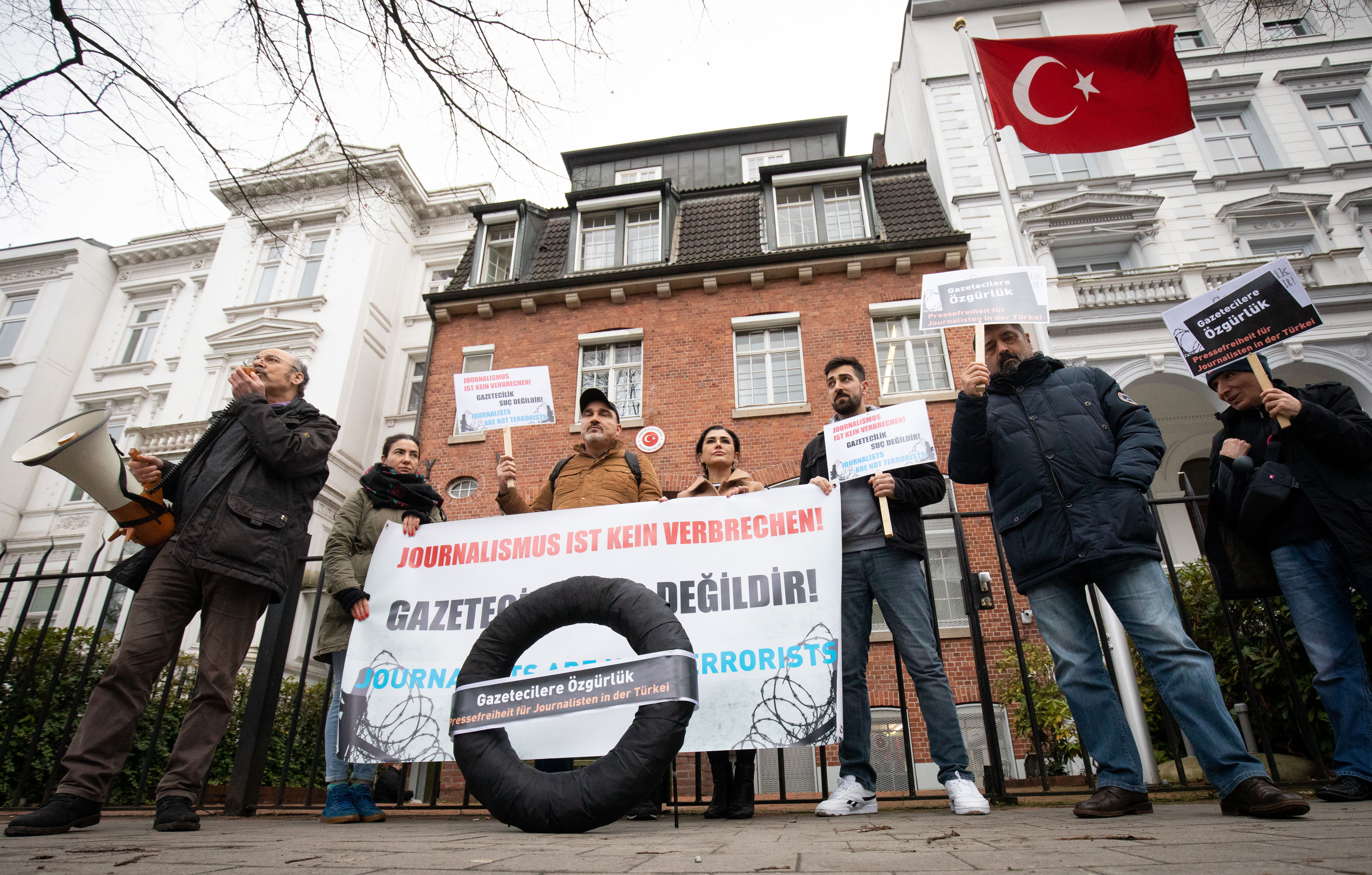 In Hamburg lebende Journalistinnen und Journalisten aus der Türkei stehen mit einem schwarzen Kranz vor dem Türkischen Konsulat.