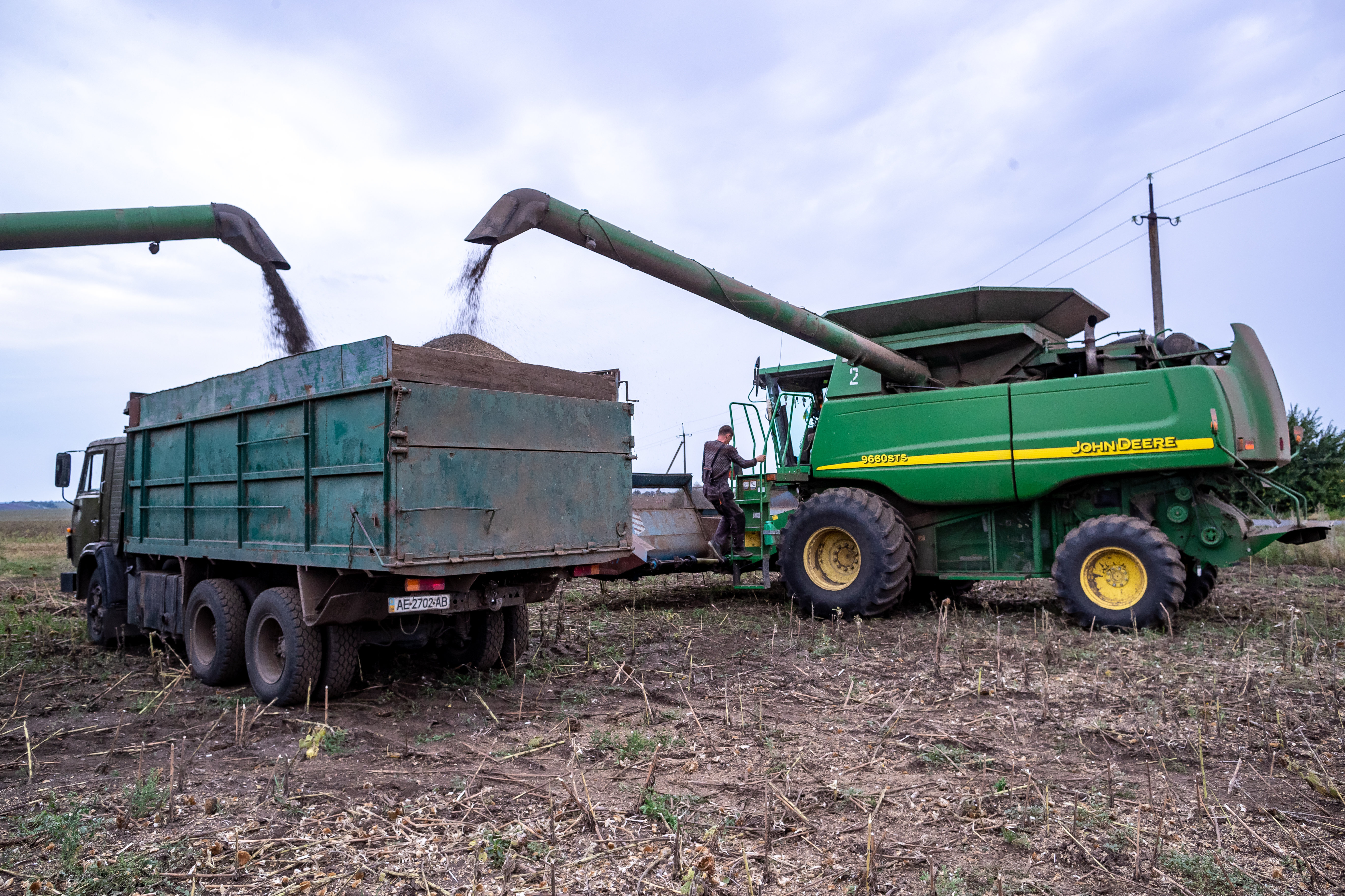 A Ukrainian farmer on a combine unloads harvested sunflower seeds onto a truck near Zaporiz'ke