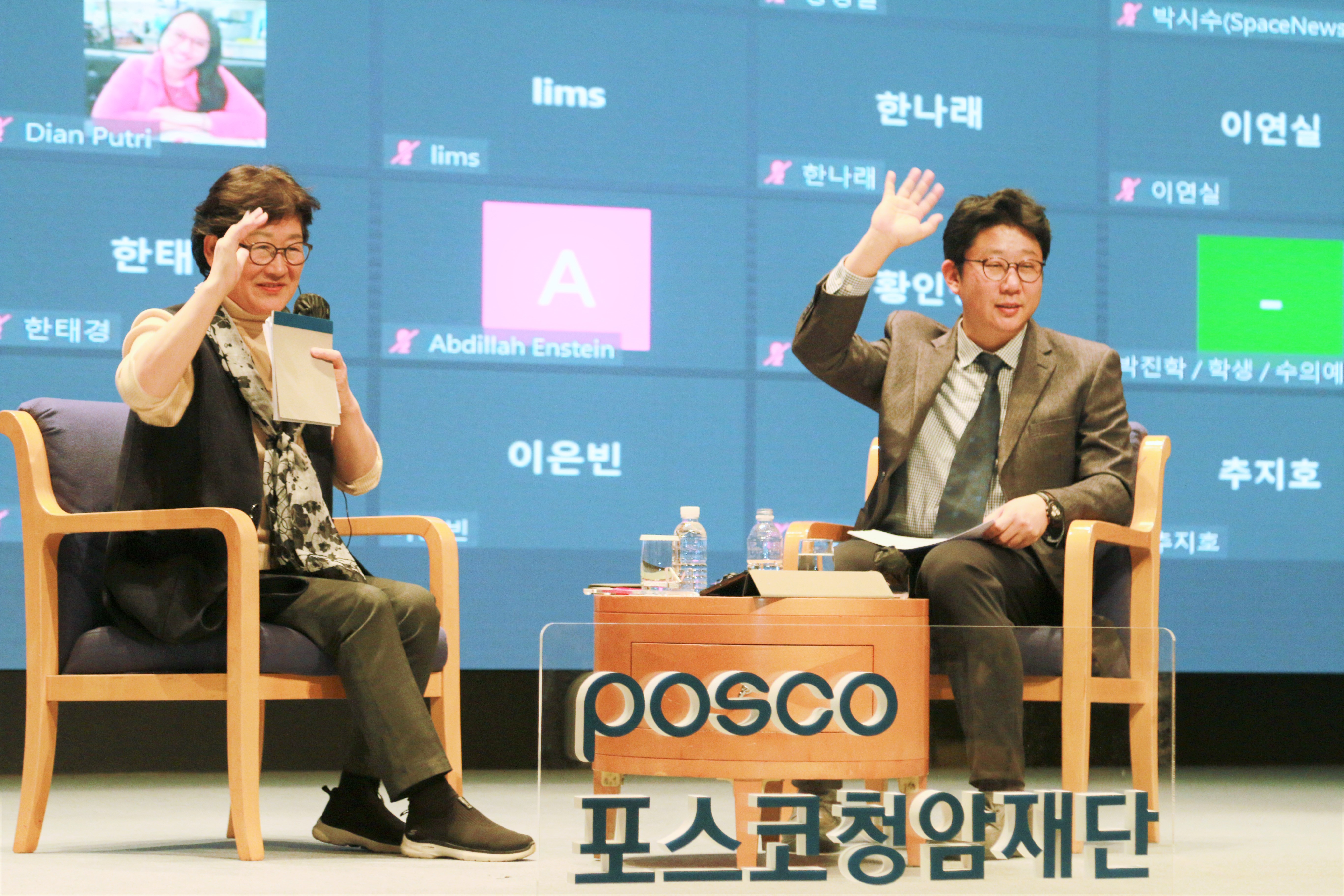 The speaker and the moderator is greeting the audience by waving their hands, smiling.