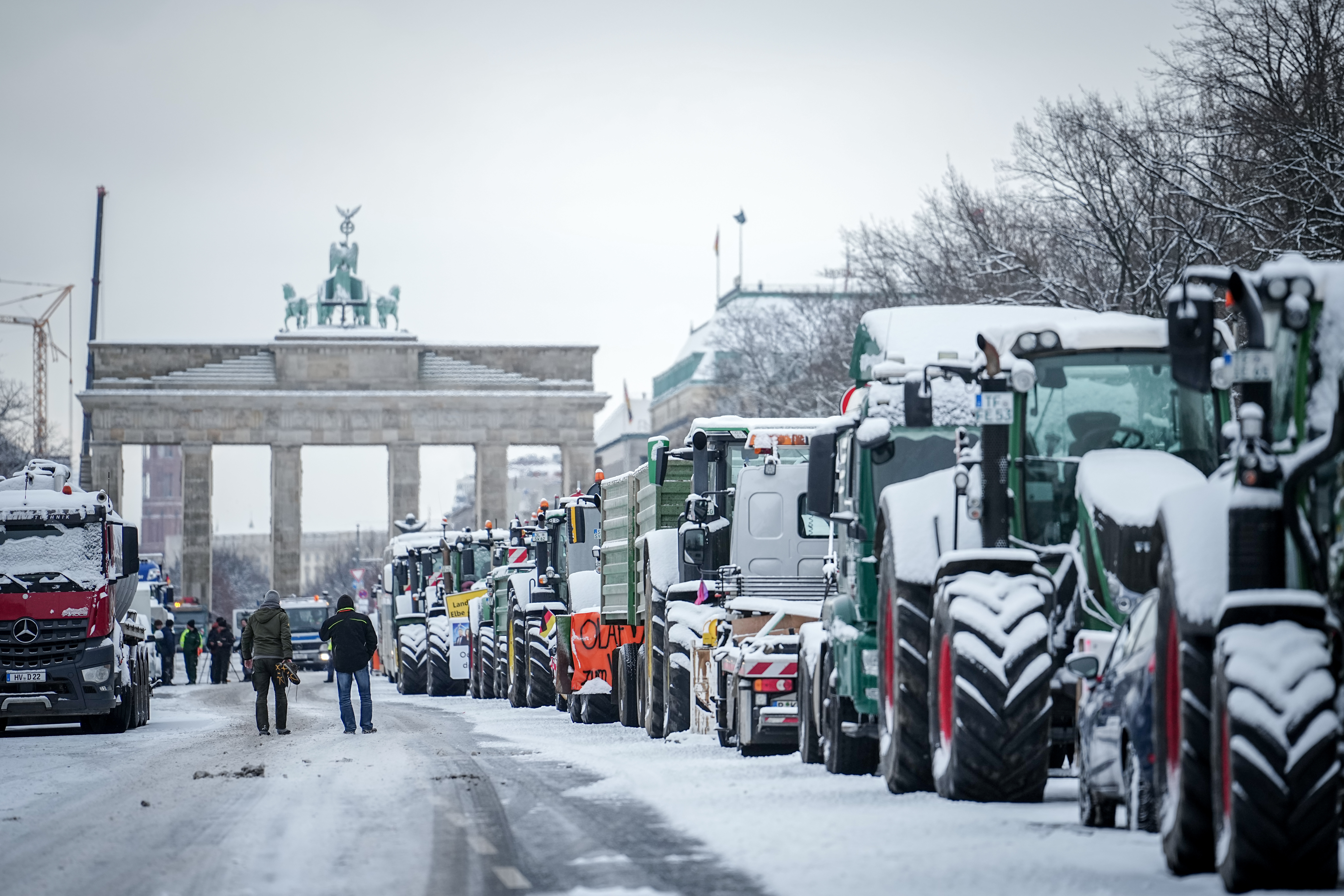 Zahlreiche schneebedeckte Traktoren stehen auf der Straße des 17. Juni vor dem Brandenburger Tor.