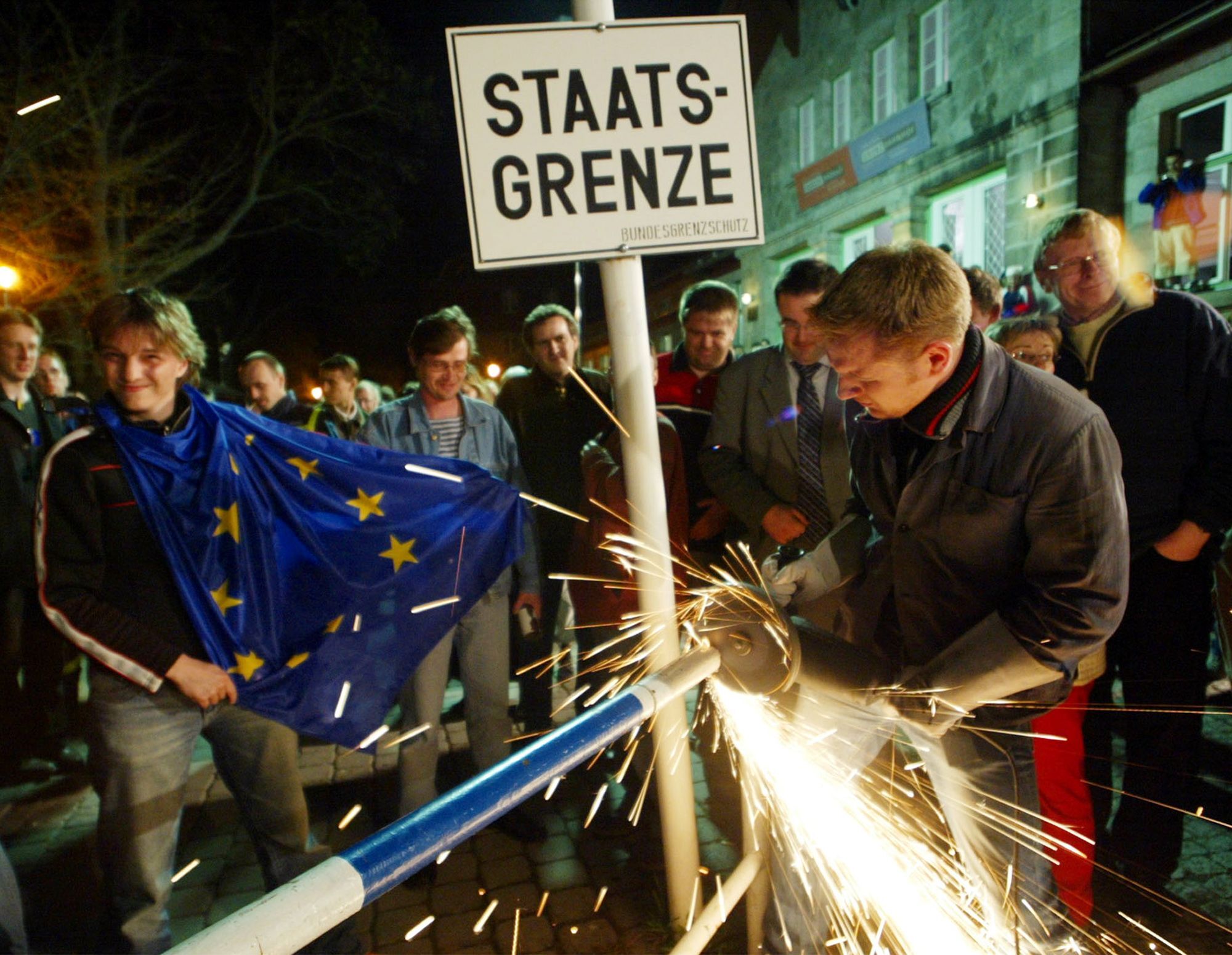 A worker removes the remains of an iron border fence dating back to the times of the Cold War at the German-Czech border in Bayerisch Eisenstein, southern Germany, Saturday, May 1, 2004, while a crowd of German and Czech people celebrates the expansion of the European Union at midnight.