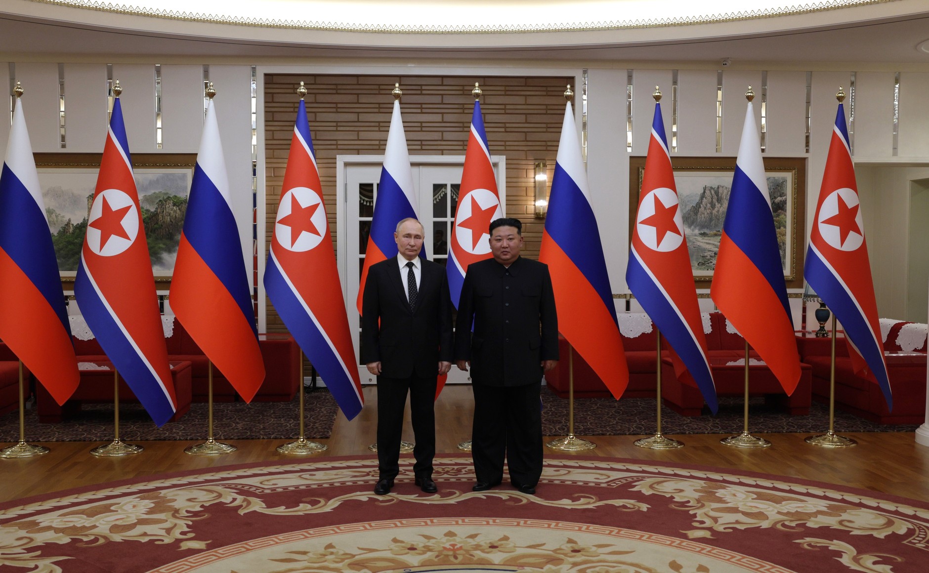 Wladimir Putin und Kim Jong Un umgeben von russischen und nordkoreanischen Flaggen.