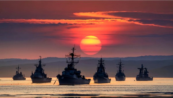 Several naval warships at sea against a sunset backdrop.