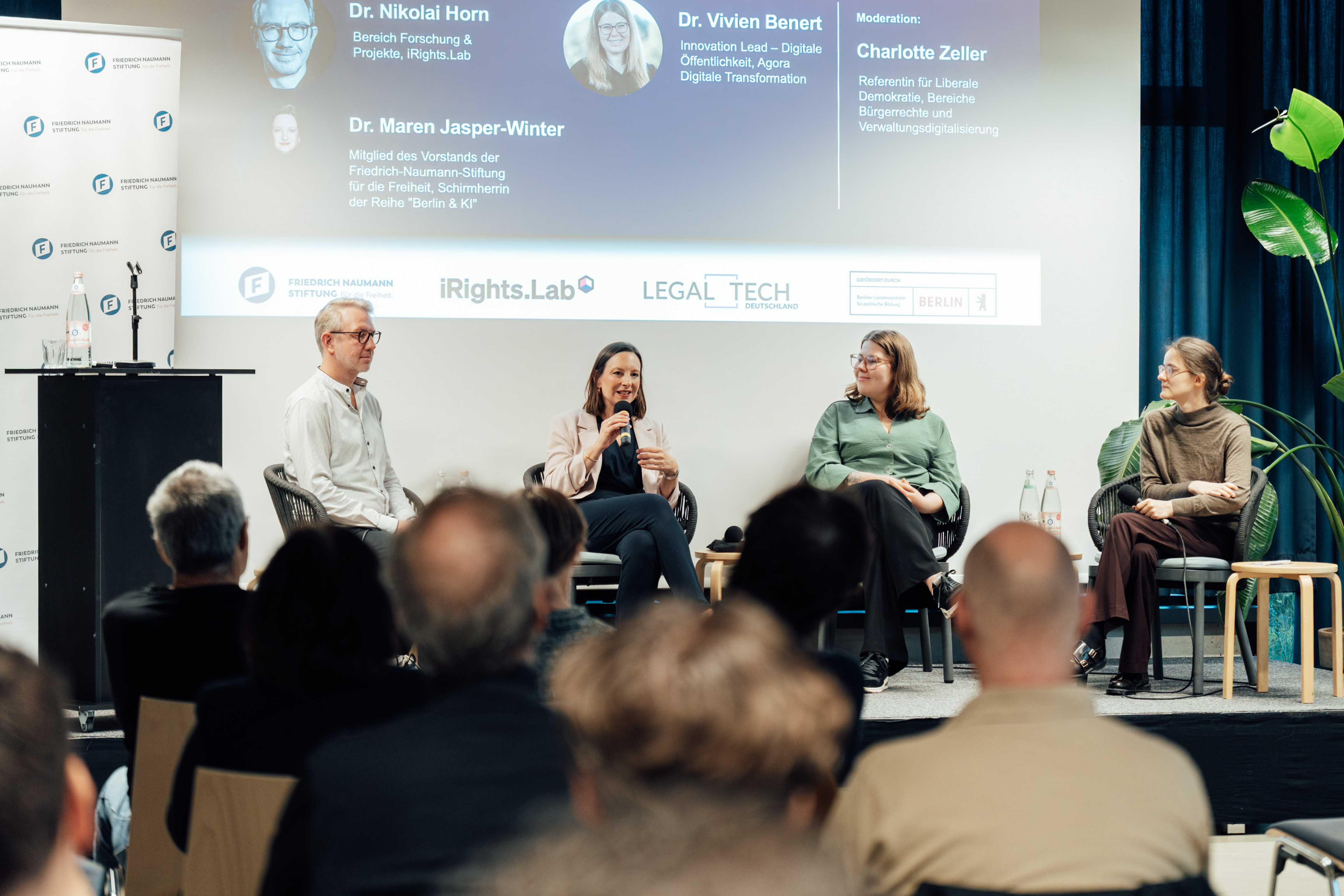 Nikolai Horn, Maren Jasper-Winter, Vivien Benert und Charlotte Zeller sitzen auf dem Podium; Maren Jasper-Winter spricht ins Mikrofon. Im Vordergrund ist das Publikum zu sehen.