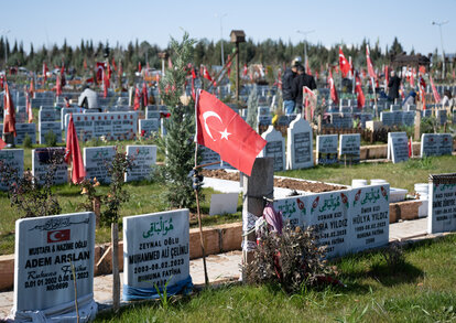 A Turkish flag waves on a burial ground in Turkey. Shortly before the first anniversary of the earthquake disaster, hundreds of relatives come to the graves of their loved ones who died in the quake on 6 February 2023