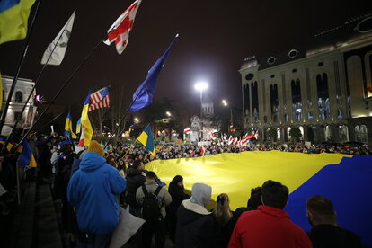 Georgier Demonstrieren mit Flaggen der EU, Ukraine und Georgiens gegen den russischen Krieg in der Ukraine auf einem Platz im Dunkeln