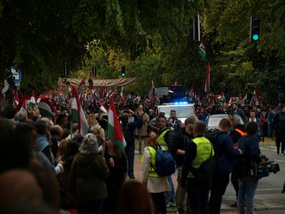 A large crowd of people gathered at a demonstration, many holding Hungarian flags in a city street.