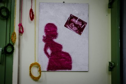 A minimalist artwork showing the silhouette of a pregnant woman in red against a white background.