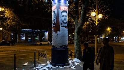 Two people walk past a quiet street scene with scattered paper.