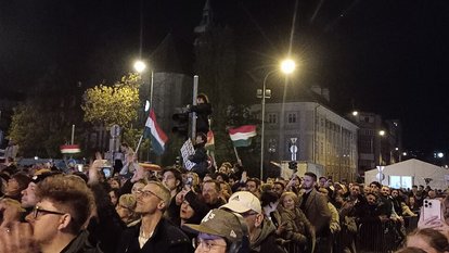 Large crowd in Budapest at night waving Hungarian flags during Péter Magyar’s victory speech.