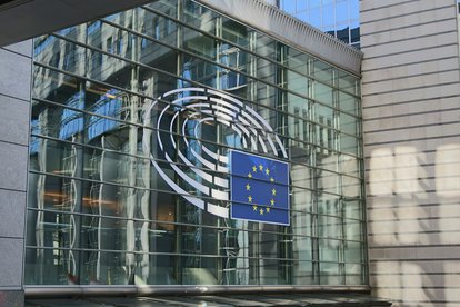 Facade of the European Parliament building in Brussels with the EU flag displayed on a glass exterior.