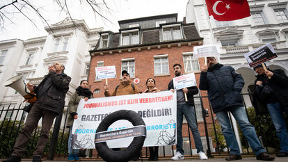 In Hamburg lebende Journalistinnen und Journalisten aus der Türkei stehen mit einem schwarzen Kranz vor dem Türkischen Konsulat.