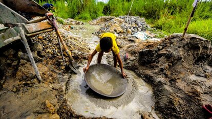 Ein Junge wäscht mit einer hölzernen Schale, die als „pabirik“ bezeichnet wird, Gold. Der Vorgang erfolgt, nachdem das Gestein vom Schlamm getrennt wurde, der im Tunnel gesammelt wurde. Gumaus, Paracale in der Provinz Camarines Norte. Foto von Juanito Bantong