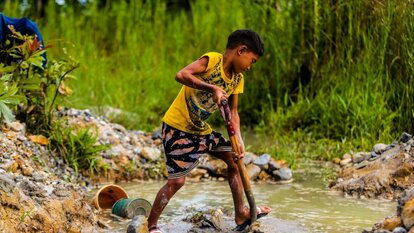 John (11) schaufelt an einem Bach schweren Schlamm, der später gewaschen wird, um das Gold heraus zu spülen. Gumaus, Paracale, Provinz Camarines Norte