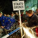 A worker removes the remains of an iron border fence dating back to the times of the Cold War at the German-Czech border in Bayerisch Eisenstein, southern Germany, Saturday, May 1, 2004, while a crowd of German and Czech people celebrates the expansion of the European Union at midnight.