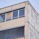 Ein Fenster des Gymnasiums am Europasportpark (GESP) ist provisorisch mit Holz verschlossen, während an den anderen Fenstern Aufkleber kleben, die anzeigen, dass diese Fenster nicht geöffnet werden dürfen. Dem Gymnasium droht wegen ausbleibender Sanierung die Schließung. 