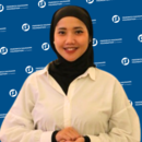 A photo of Nurul Fitriani with FNF background in blue. She wears white shirt and black hijab.