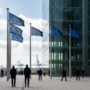 EU‑Flaggen vor modernem Institutionsgebäude in Brüssel, mit subtilen Logistik‑Elementen im Hintergrund.