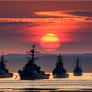 Several naval warships at sea against a sunset backdrop.