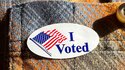 Ein "Ich habe gewählt" Sticker wird am Wahltag auf das Hemd einer Person gesteckt.