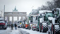 Zahlreiche schneebedeckte Traktoren stehen auf der Straße des 17. Juni vor dem Brandenburger Tor.