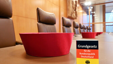 Auf der Richterbank im Sitzungssaal im Bundesverfassungsgericht liegen Barette der Bundesverfassungsrichter des ersten Senats. Dabei ist eine Miniaturausgabe des Grundgesetz für die Bundesrepublik Deutschland zu sehen. Im September 2021 feiert das Bundesverfassungsgericht seinen 70. Geburtstag.