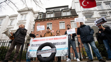 In Hamburg lebende Journalistinnen und Journalisten aus der Türkei stehen mit einem schwarzen Kranz vor dem Türkischen Konsulat.