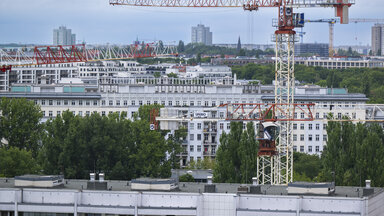 Baukräne ragen in den Himmel vor der Kulisse der Wohnhäuser im Berliner Osten. 