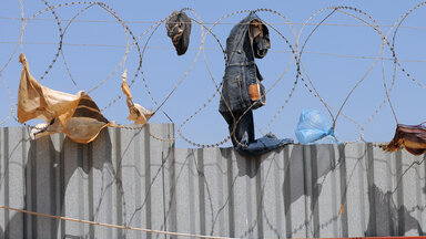 Kleidung wurde offensichtlich über eine mit NATO-Draht gesicherte Mauer in ein Lager für Binnnevertriebene in der libyschen Hauptstadt Tripolis geworfen und blieb im Stacheldraht hängen