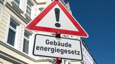 Warnschild "Gefahrstelle" (Zeichen 101) und ein Zusatzschild mit der Aufschrift "Gebäudeenergiegesetz".