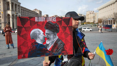Ukrainischer Demonstrant hält Bild von Putin und Ayatollah beim Küssen