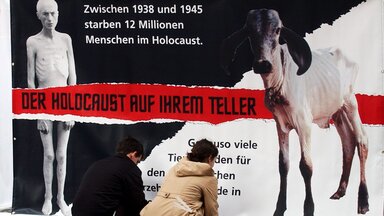 Mitglieder der internationalen Tierrechtsorganisation Peta befestigen ein Poster, das einen abgemagerten jüdischen Gefangenen in einem Konzentrationslager sowie ein kurz vor dem Tod stehendes Kalb zeigt.  Mitglieder der internationalen Tierrechtsorganisation Peta befestigen ein Poster, das einen abgemagerten jüdischen Gefangenen in einem Konzentrationslager sowie ein kurz vor dem Tod stehendes Kalb zeigt.
