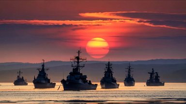 Several naval warships at sea against a sunset backdrop.