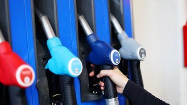 Eine Kundin an einer Tankstelle greift nach der Zapfpistole in einer Zapfsäule. 