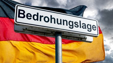 Warnschild ‚Bedrohungslage‘ vor der deutschen Flagge