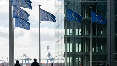 EU‑Flaggen vor modernem Institutionsgebäude in Brüssel, mit subtilen Logistik‑Elementen im Hintergrund.