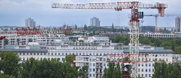 Baukräne ragen in den Himmel vor der Kulisse der Wohnhäuser im Berliner Osten. 