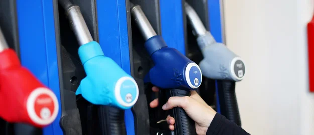 Eine Kundin an einer Tankstelle greift nach der Zapfpistole in einer Zapfsäule. 