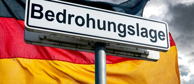 Warnschild ‚Bedrohungslage‘ vor der deutschen Flagge